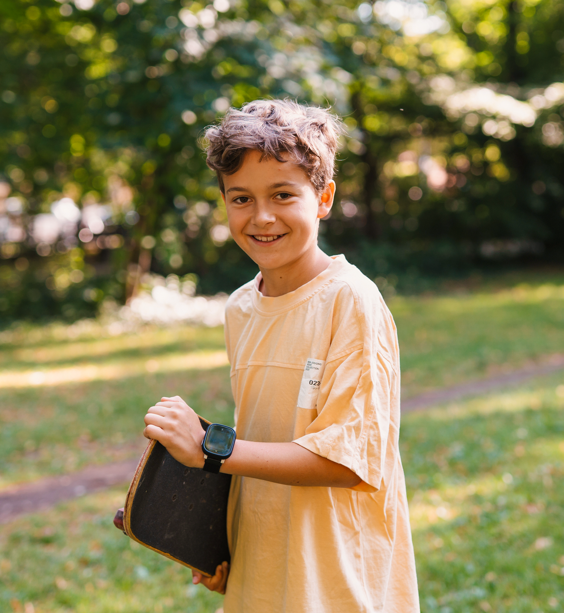 Young boy holding a skateboard outdoors in a park